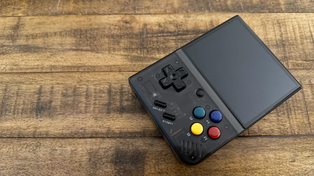 A semi-transparent handheld gaming device with four colorful buttons against a wooden background.